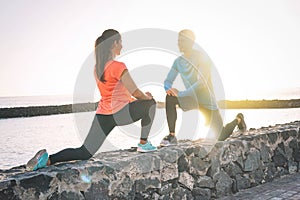 Young health couple stretching legs next to the beach at sunset - Happy sportive lovers workout together