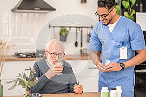 Young healthcare worker observing a pensioner swallowing down a medication