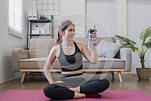 Young healthy Asian woman holds a water bottle for practicing yoga online or exercising at home.