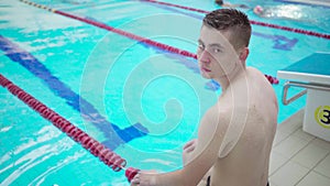 Young healthy athletic guy after jumping and diving sit near indoor swimming pool on a swimming track. Healthy lifestyle