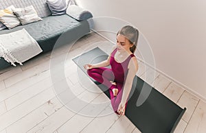 Young healthy beautiful woman practicing yoga at home sitting in lotus pose on yoga mat meditating relaxed. Indoor and