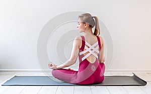 Young healthy beautiful woman practicing yoga at home sitting in lotus pose on yoga mat meditating relaxed. Indoor and