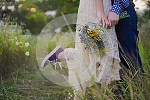 Young healthy couple fashionable girl in a wedding dress guy in a plaid shirt standing with a bouquet of bright flowers in hands,