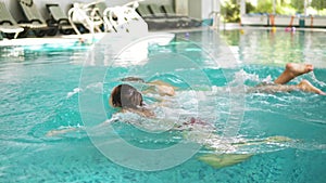 Young healthy family together with their child are diving under the water in the swimming pool holding hands. Mother and