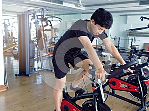 Young healthy man exercising on bike machine at sport gym. Fitness and workout concept