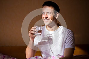 Young healthy man stretching after sleep with glass of water