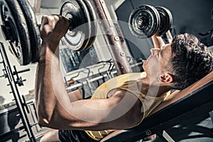 Young healthy man trains his chest lifting dumbbells