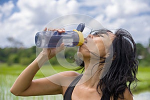 Young healthy sporty Asian Chinese woman drinking water bottle after fitness training and running workout outdoors on green field