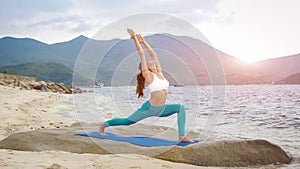 Young healthy sporty woman practicing yoga on the beach at sunset.