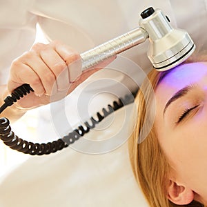 Young healthy woman with good skin doing cosmetic procedures in spa clinic. Light treatment.