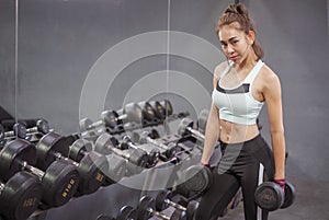 Young healthy woman lifting dumbbells in fitness gym