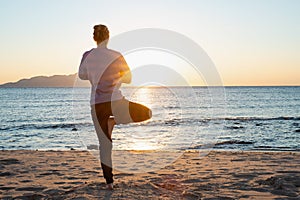 Young healthy woman practicing yoga on the beach at sunrise