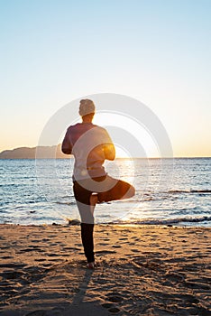 Young healthy woman practicing yoga on the beach at sunrise