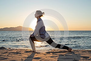 Young healthy woman practicing yoga on the beach at sunrise