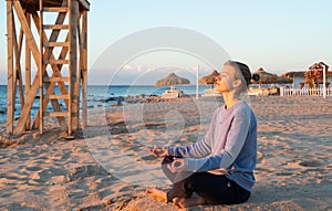 Young healthy woman practicing yoga on the beach at sunrise