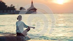 Young healthy woman practicing yoga on the beach at sunset