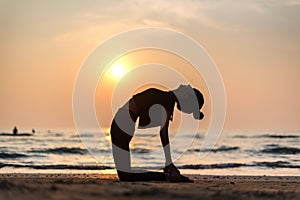 Young healthy woman practicing yoga on the beach at sunset