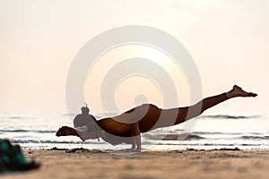 Young healthy woman practicing yoga on the beach at sunset