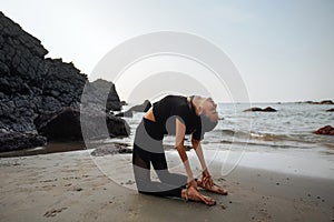 Young healthy woman practicing yoga on the beach at sunset