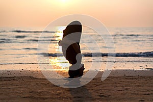 Young healthy woman practicing yoga on the beach at sunset