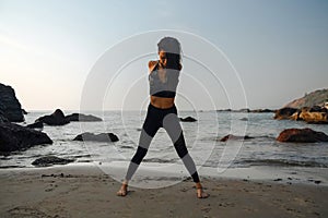 Young healthy woman practicing yoga on the beach at sunset