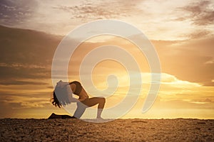 Young healthy woman practicing yoga on the beach at sunset.