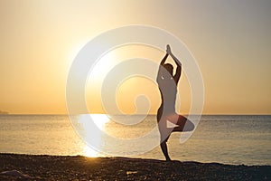 Young healthy woman practicing yoga on the beach at sunset