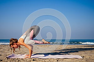 Young healthy woman in a stylish one-piece jumpsuit practicing yoga on the beach at sunrise