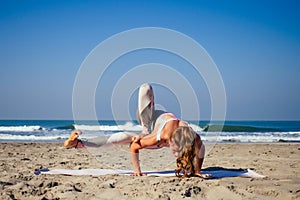Young healthy woman in a stylish one-piece jumpsuit practicing yoga on the beach at sunrise