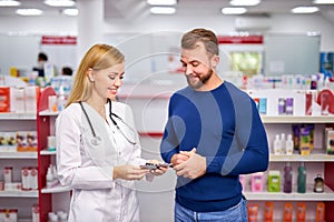 Young helpful female druggist dealing with a male customer, explaining a prescription