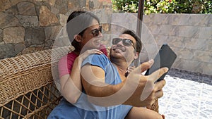 Young heterosexual couple making fun while take a selfie with a smart phone. Husban and Wife tenderness in a couch comfortable