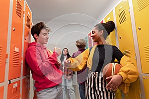 Young high school students meeting and greeting near locker in campus hallway talking and high fiving.