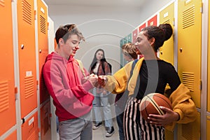 Young high school students meeting and greeting near locker in campus hallway talking and high fiving.