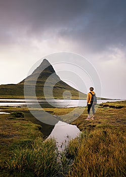 Young hiker with a backpack looks at the Kirkjufell mountain in Iceland