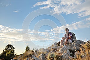 Young hiker with backpack sitting on a rock on the top of a mountain