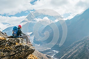 Young hiker backpacker female sitting on the cliff edge and enjoying Ama Dablam 6,812m peak view during Everest Base Camp EBC