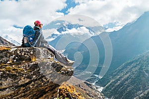Young hiker backpacker female sitting on the cliff edge and enjoying Ama Dablam 6,812m peak view during Everest Base Camp EBC