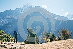 Young hiker backpacker man using trekking poles enjoying the Thamserku 6608m mountain with flying rescue helicopter during high