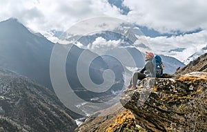 Young hiker female backpacker sitting on the cliff edge and enjoying mountain peaks view during Everest Base Camp EBC trekking