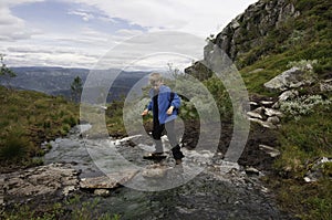 Young hiker jumping over mountain river