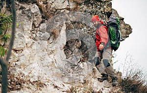 Young hiker male hiking in mountains wearing red clothes exploring new place. Traveler bearded man trekking and mountaineering