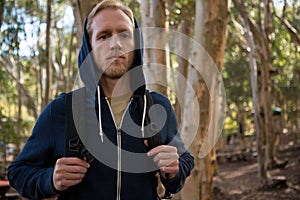 Young hiker man with backpack standing in the forest on a sunny day