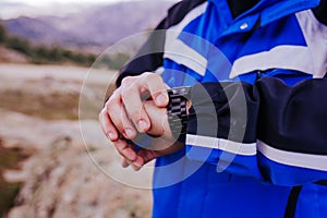 young hiker man checking smart watch on top of the mountain. cloudy day