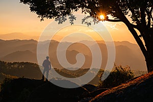 Young hiker man standing on top of mountain with the sun in the sunset