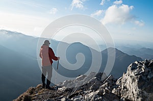 Young hiker Man standing with trekking poles on cliff edge and looking at Tatra mountains valley. Successful summit concept image.