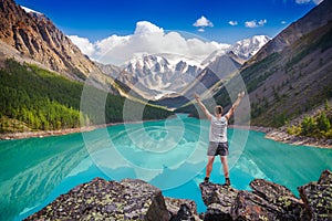 Young hiker standing with raised hands near the beautiful mountain lake and enjoying valley view
