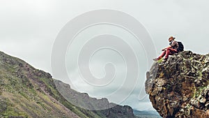 Young hiker traveler man sitting on top and enjoy view of mountain summer spring valley, copy-space. Adventure wanderlust