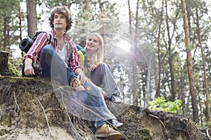 Young hiking couple sitting on edge of cliff in forest