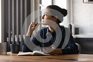 Young hindu female studying by desk looking aside holding phone