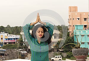 A young Hindu woman standing in an open environment, closing her eyes and folding her hands above the head to the Sun God